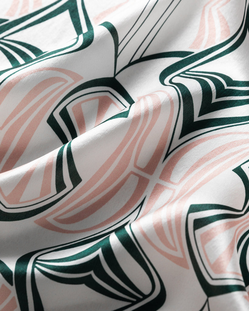 Closeup image of a silk scarf printed with a dusky pink and forest green art nouveau pattern