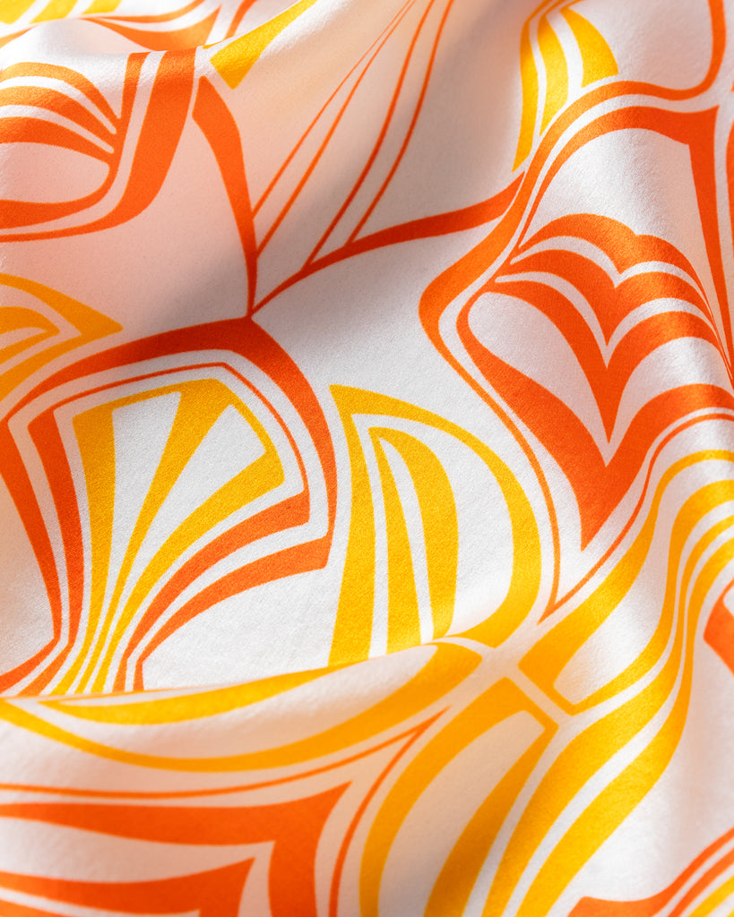 Closeup image of a silk scarf printed with a bright orange and yellow art nouveau pattern