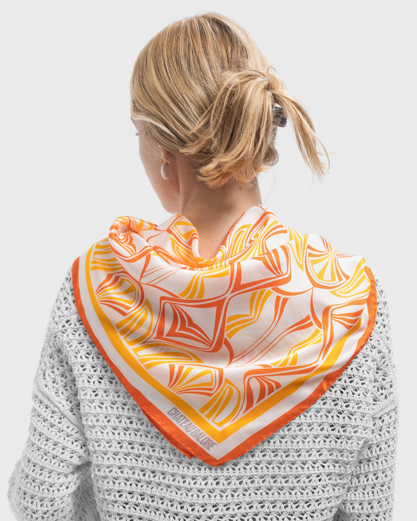 Backview of a blonde woman wearing a silk scarf with a art nouveau inspired pattern